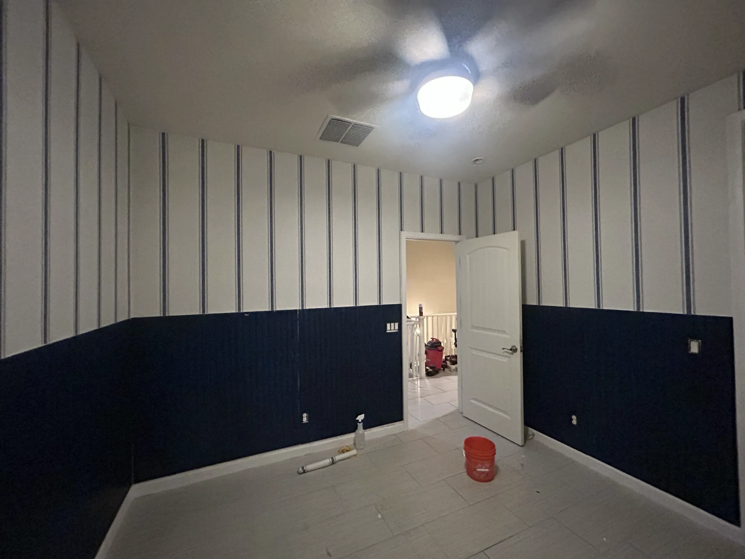 A room mid-job: pinstripe paper above navy panelling, tools on the floor