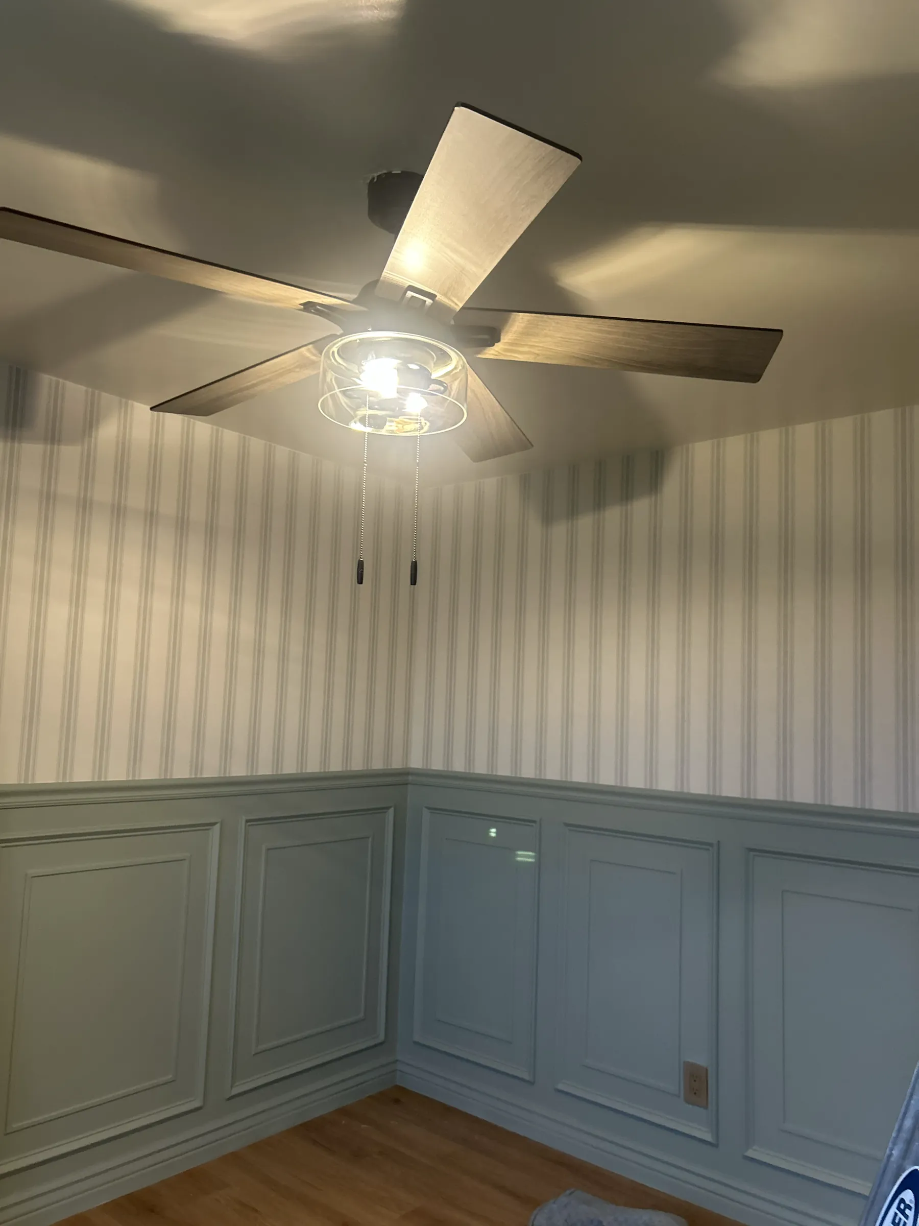 A ticking stripe above pale blue wall panelling, under a ceiling fan
