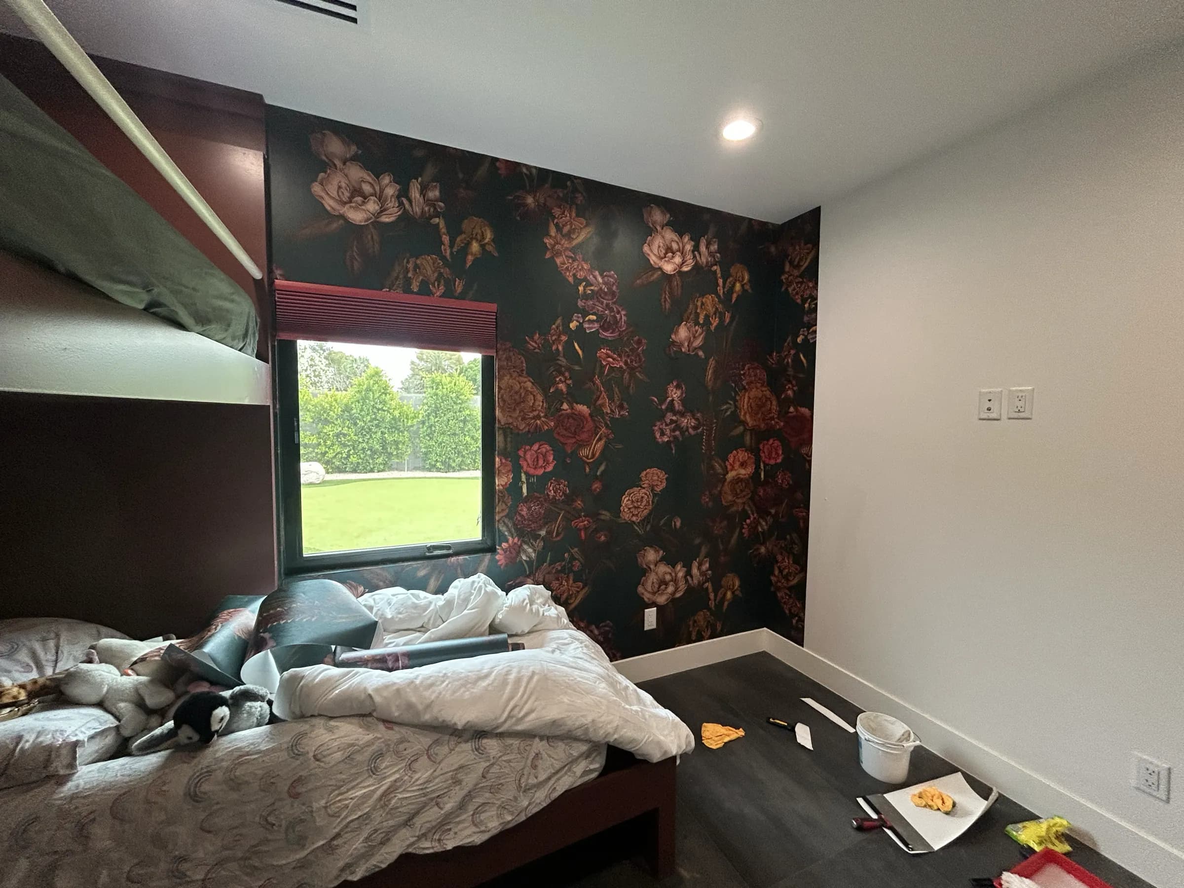 A bedroom mid-install: dark floral paper on two walls, the third still bare