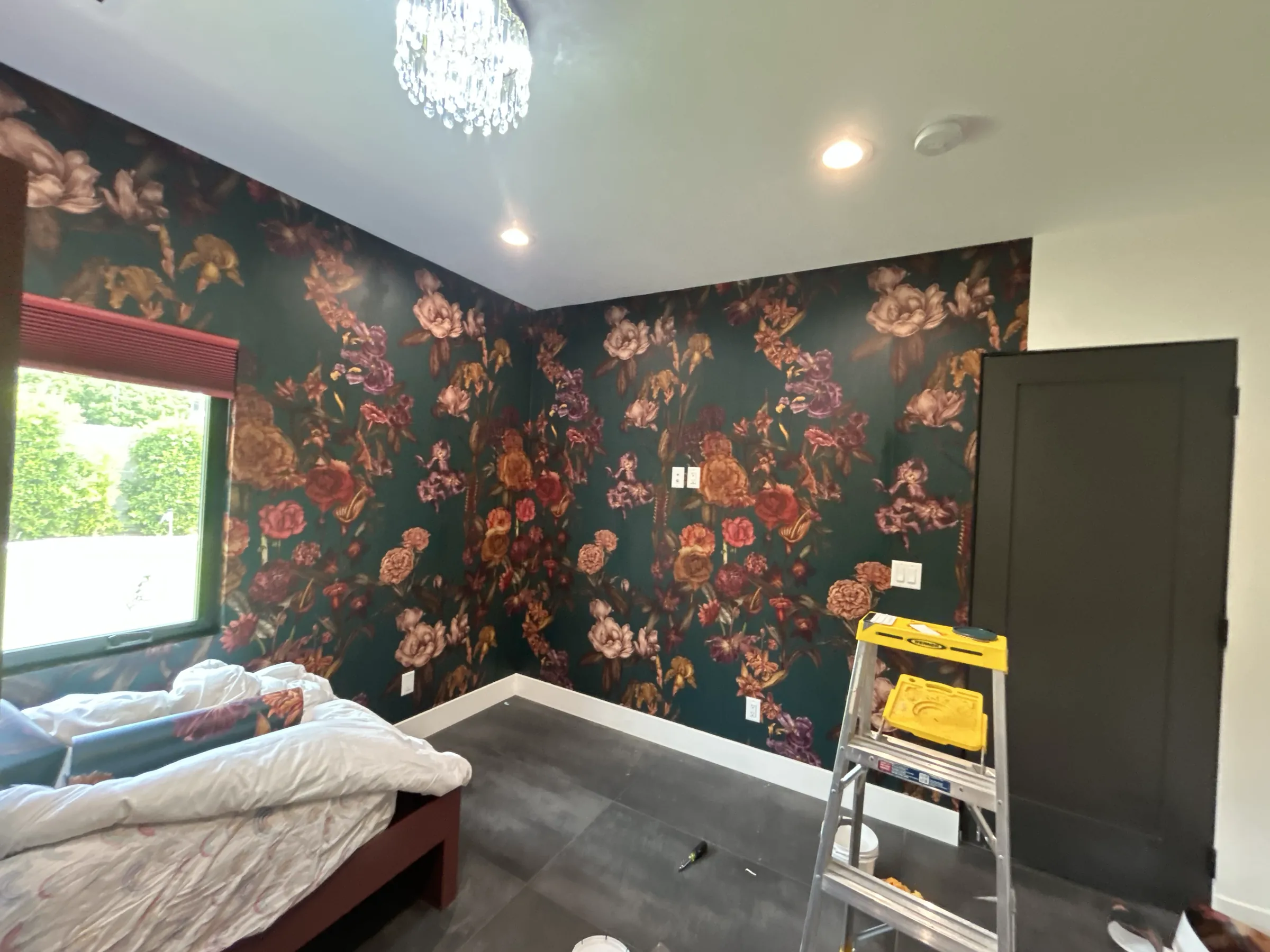 Dark floral wallpaper going up in a bedroom, a stepladder in the middle of the room