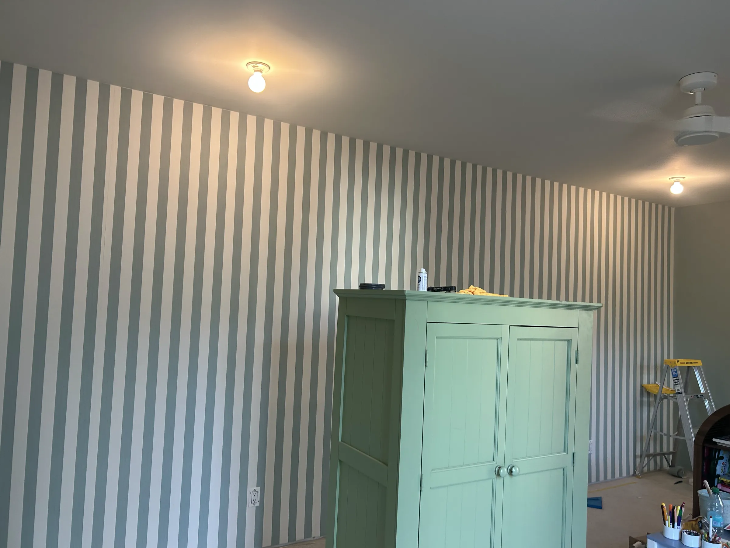 A playroom with wide sage and white stripes behind a green armoire