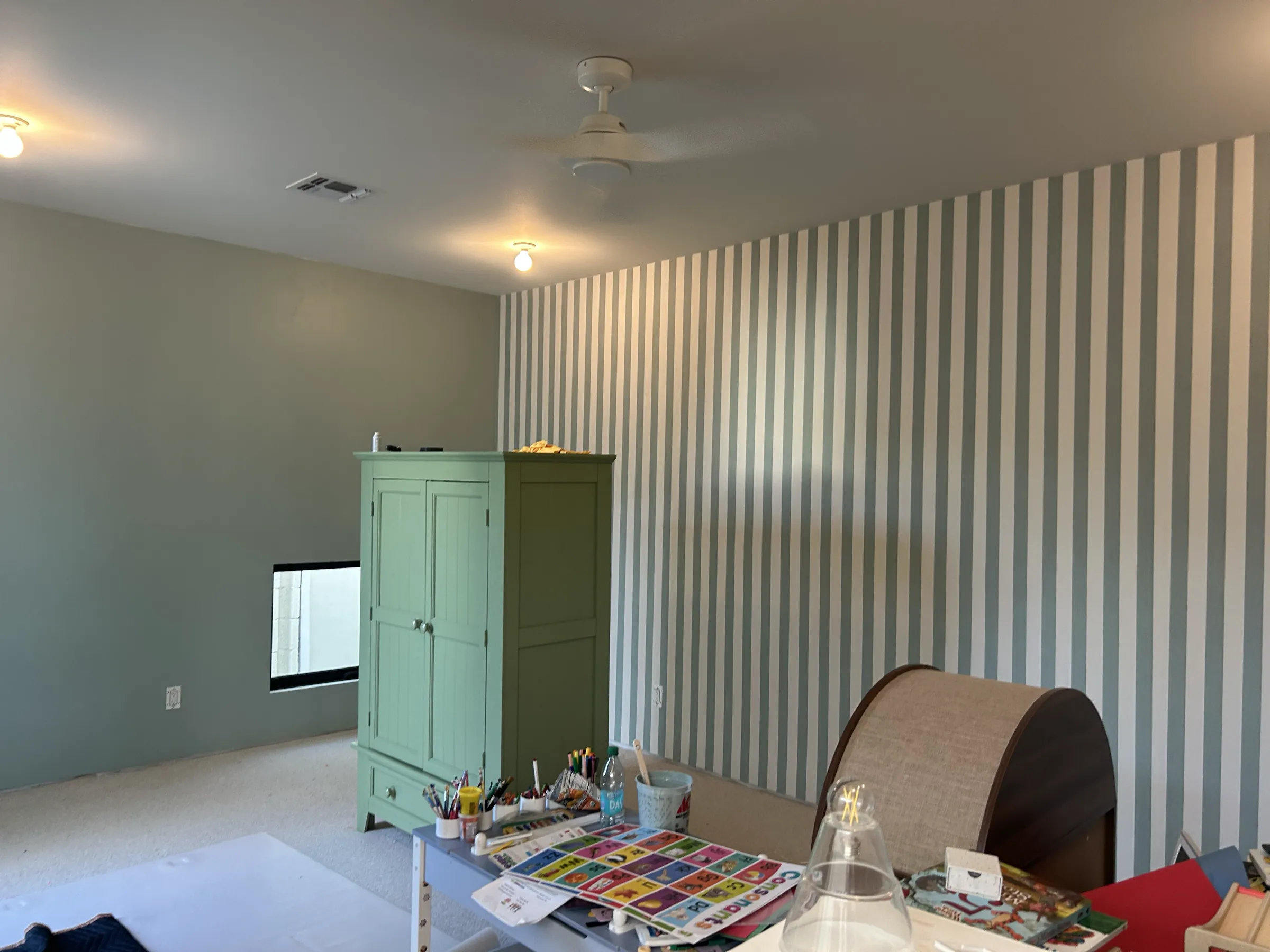 A wider view of the sage-striped playroom with its green armoire