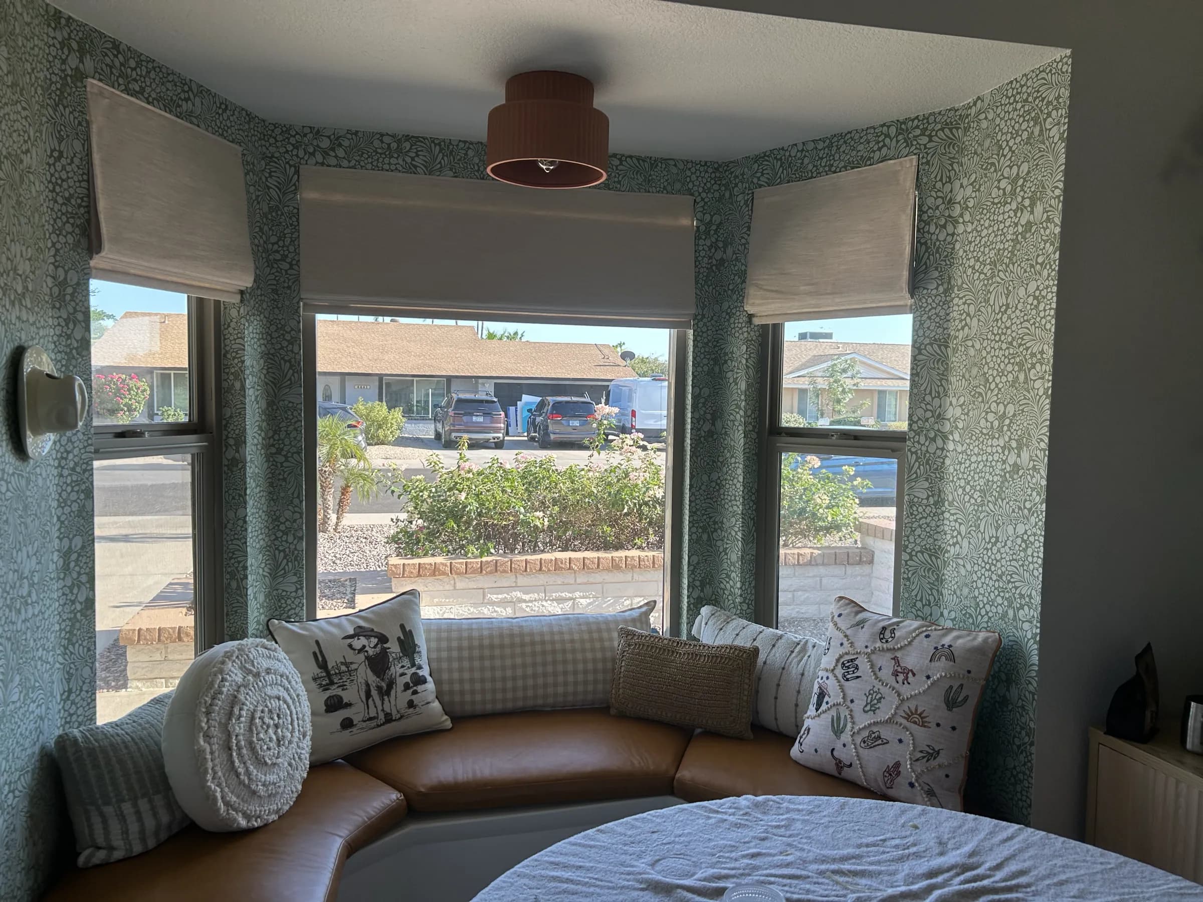 A bay window seat wrapped in green botanical wallpaper
