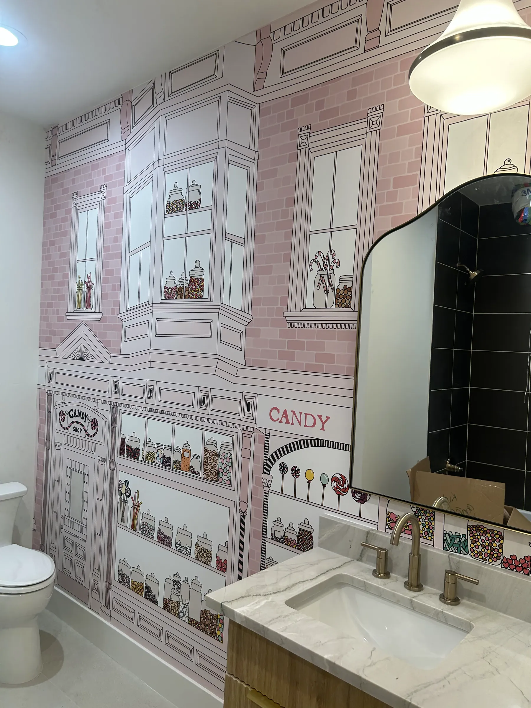 A bathroom with a pink candy-shop storefront mural behind the vanity