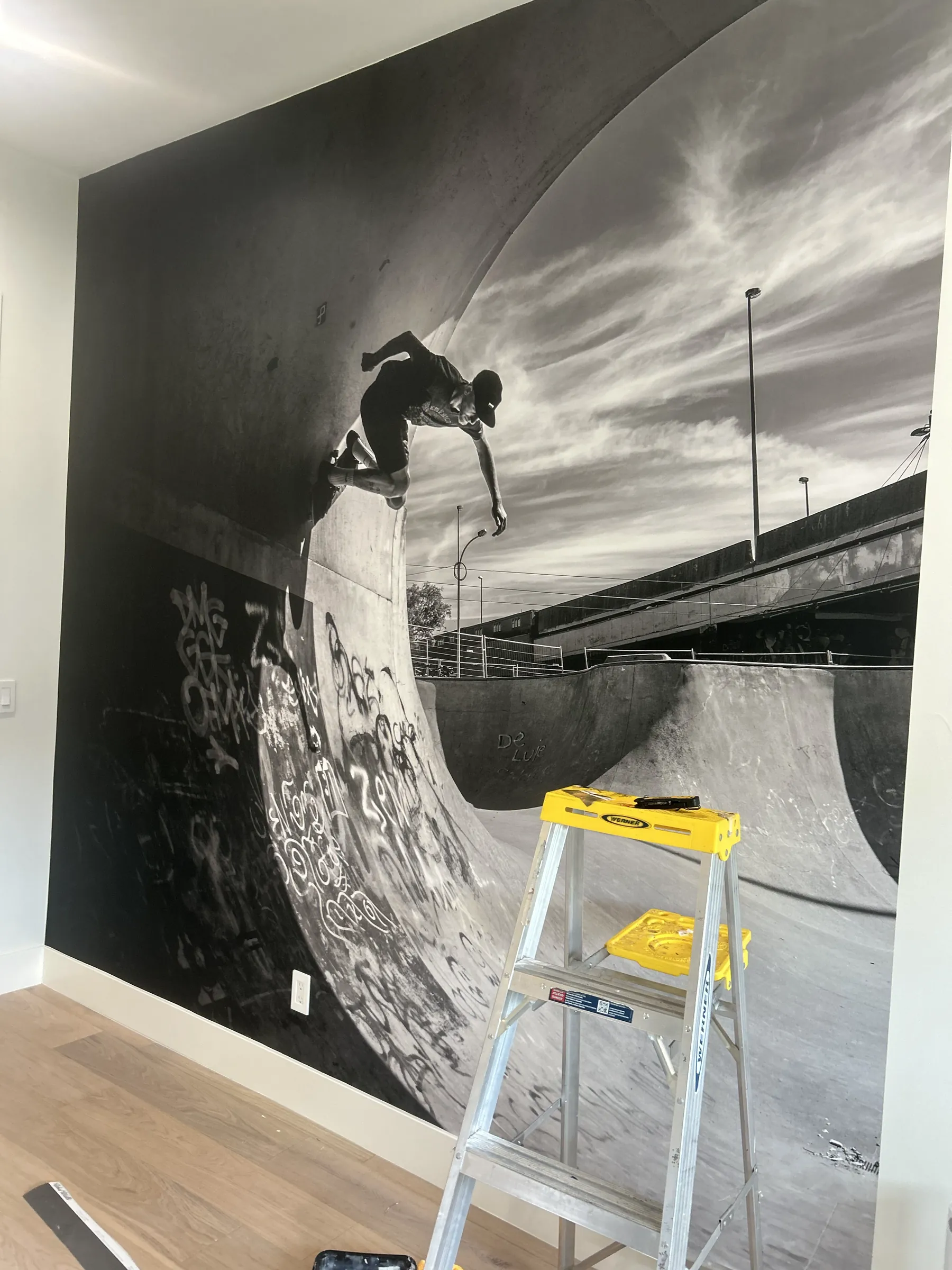 A floor-to-ceiling black and white skateboarding mural with a stepladder in front