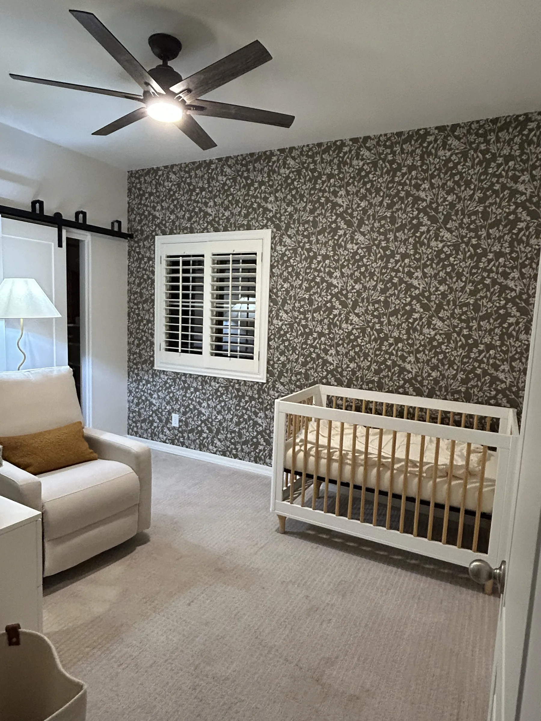 A nursery with a charcoal leaf-print feature wall above the crib